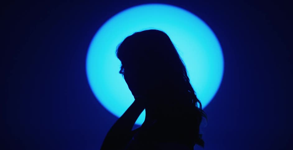 Female model touching her wavy hair is silhouetted against the spotlight in the studio