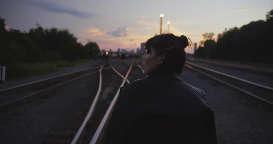 After looking around woman walks along train tracks toward city skyline