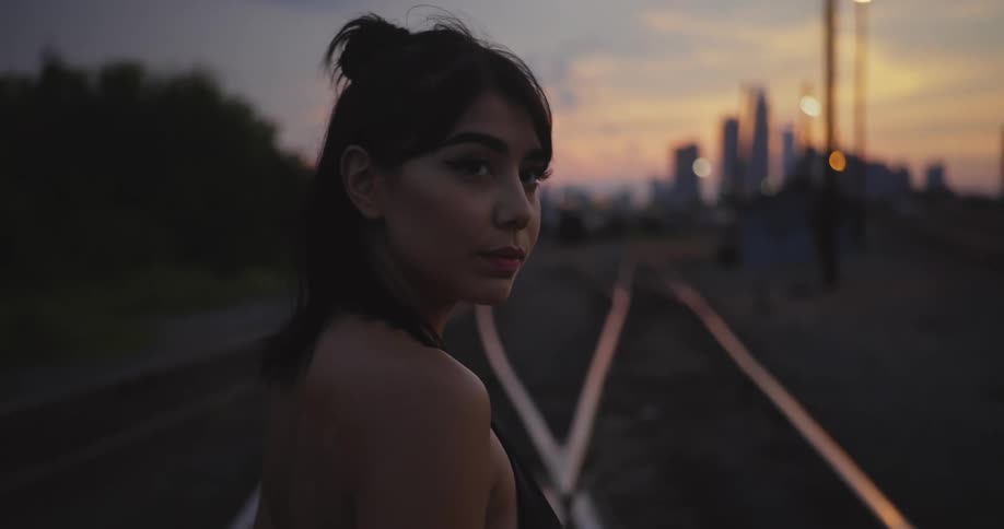 A female brunette is standing outside near railroad tracks