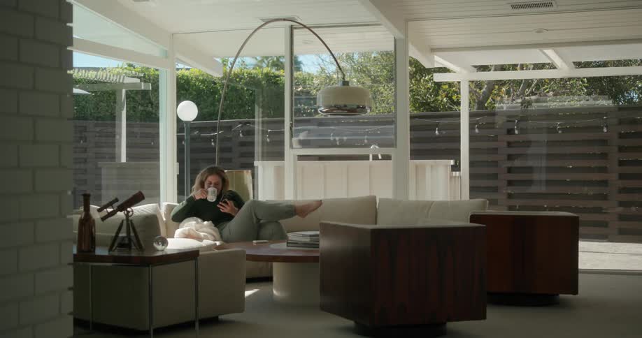 Woman sitting on the sofa in her living room and using her smartphone and having a cup of coffee