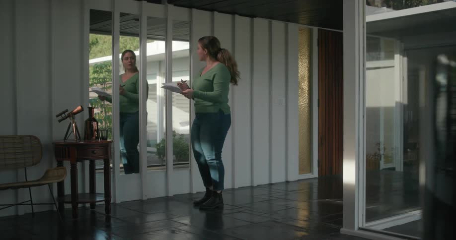 A woman walking through a hallway and stopping in front of mirrors hung on the wall