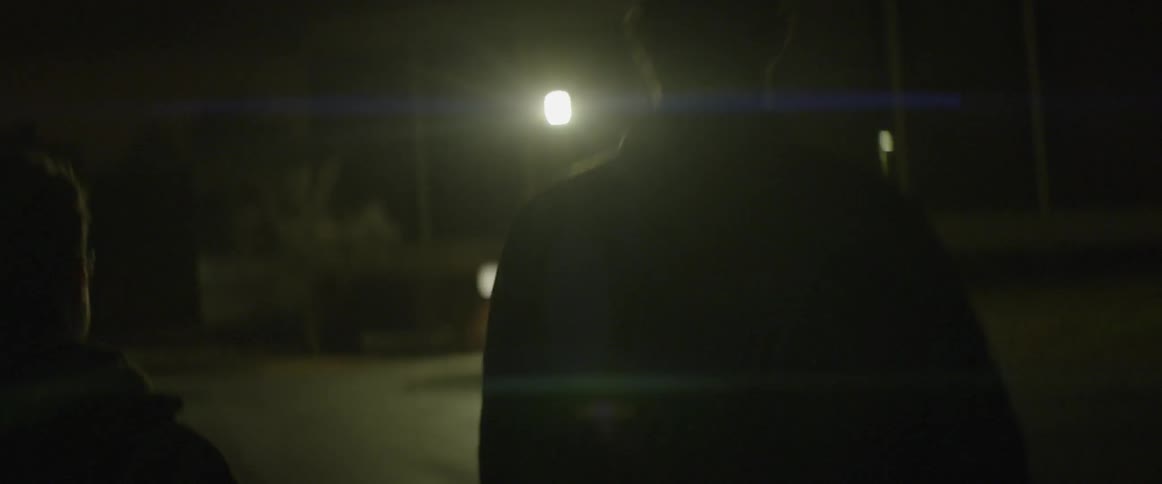 Two men walk down a well lit street at night