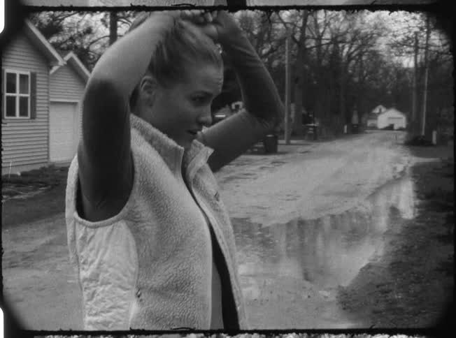 A woman in a ponytail rubs her head and stands up