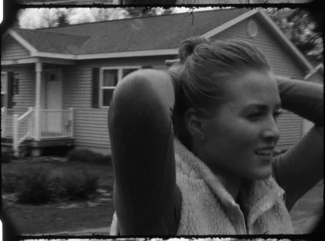 A woman in a ponytail and a vest stands outside