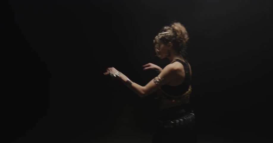 Belly dancer wearing bedlahheadbands with golden coins golden necklace and bracelets performs dance on stage