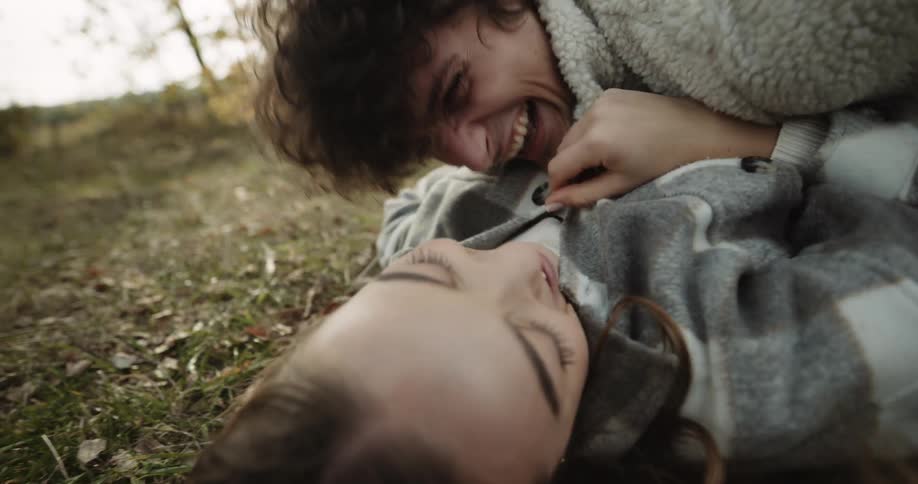 A man and woman playfully rolling around on the ground smiling and laughing