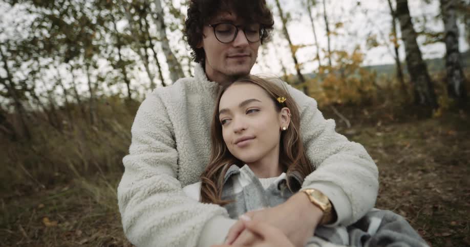 A teenage boy and girl hugging and cuddling outside on the ground on a fall day