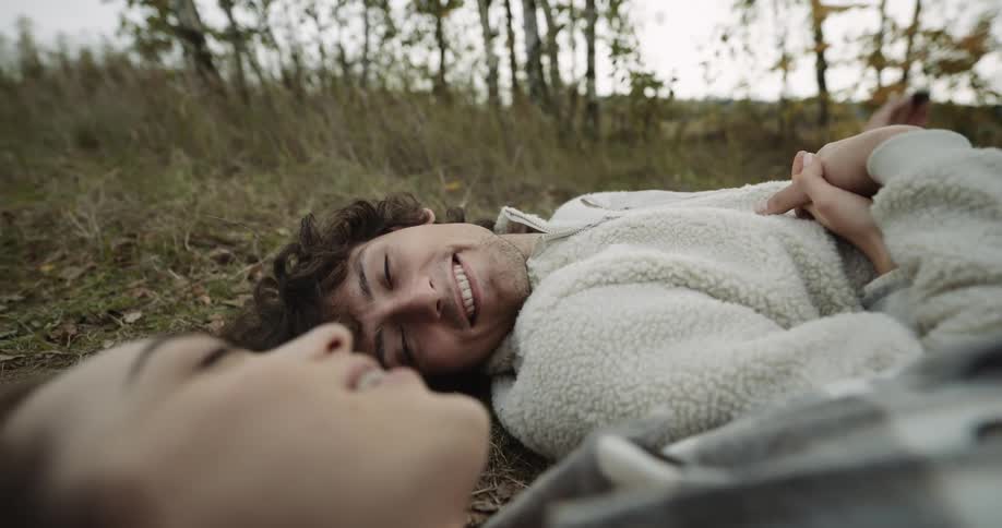 A teenage boy and girl holding hands and flirting while lying on the ground outside