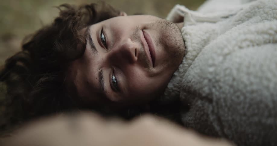A young man smiling while lying on the ground outside and chatting with a girl