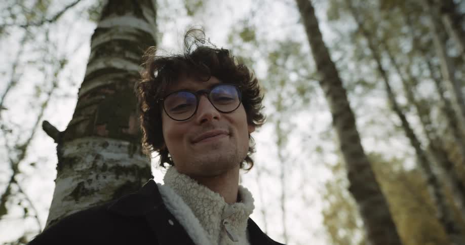 Man smiles while leaning against tree in woods on a sunny day