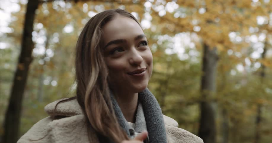 A teenage girl has a smile on her face as she stands in the woods and plays with her long hair