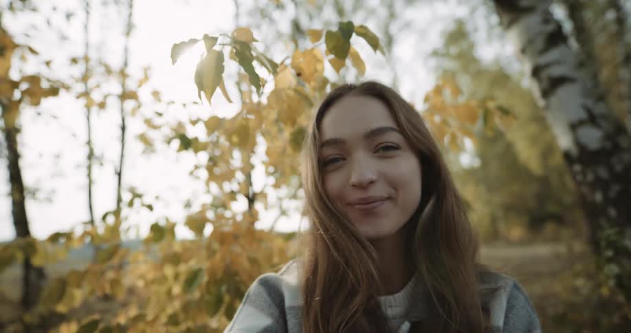 A teenage girl smiling and laughing next to trees in autumn