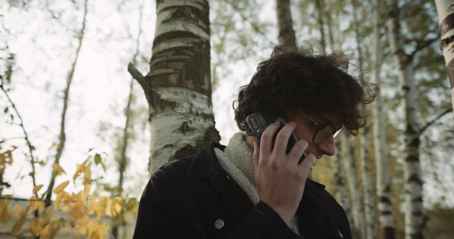 A man talks on the phone while leaning against a tree in the forest