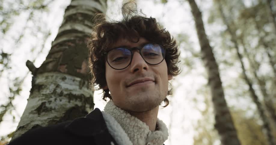 A man smiling while leaning against a tree in a forest