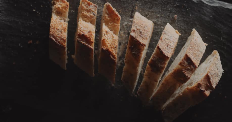 A loaf of bread sits in a row of slices on a platter