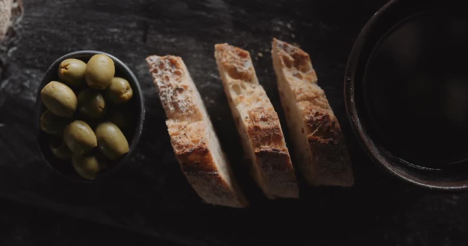 Slices of bread sit next to a bowl of olives on a serving platter