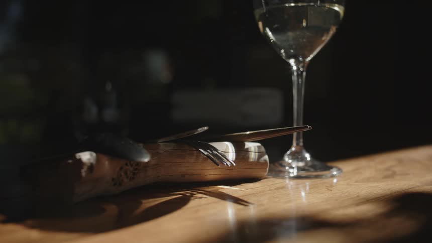 A close up of a glass of wine next to a knife fork and spoons on a wooden table