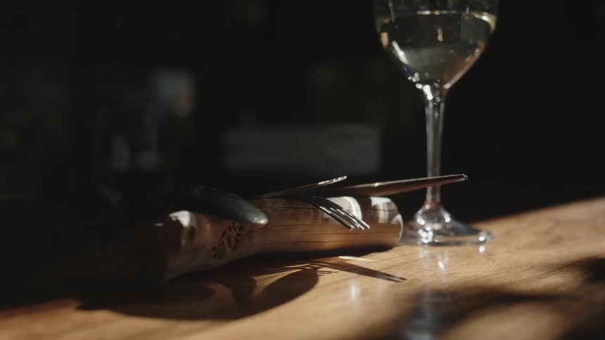A wine glass and utensils are sitting on a counter top in a bar near a window