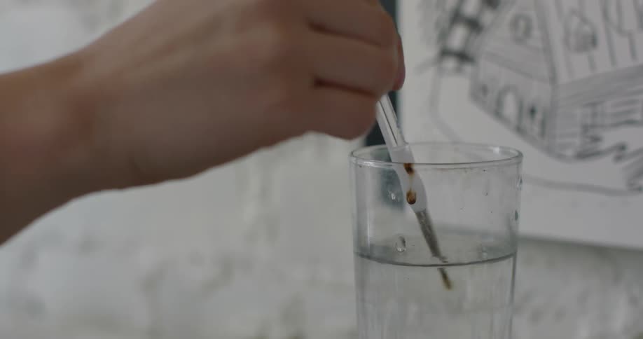 A female hand with a paint brush dips the paint brush in a glass of water