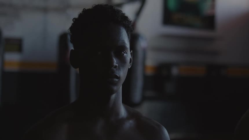 Two Brazilian boxer stand in front of boxing bags in dimly lit boxing gym