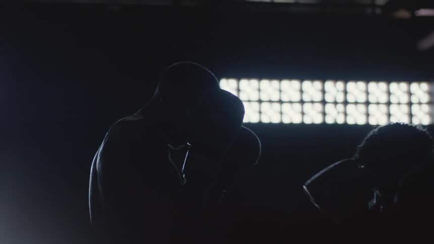 Two men are boxing in a dark room illuminated by light coming in from the windows