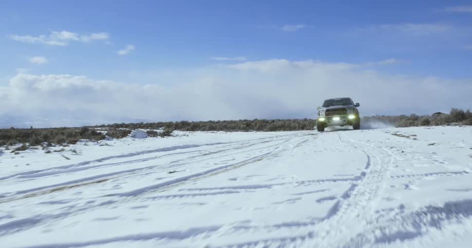 A large pickup truck is speeding on a flat snowy terrain sliding and drifting as it passes by during the day