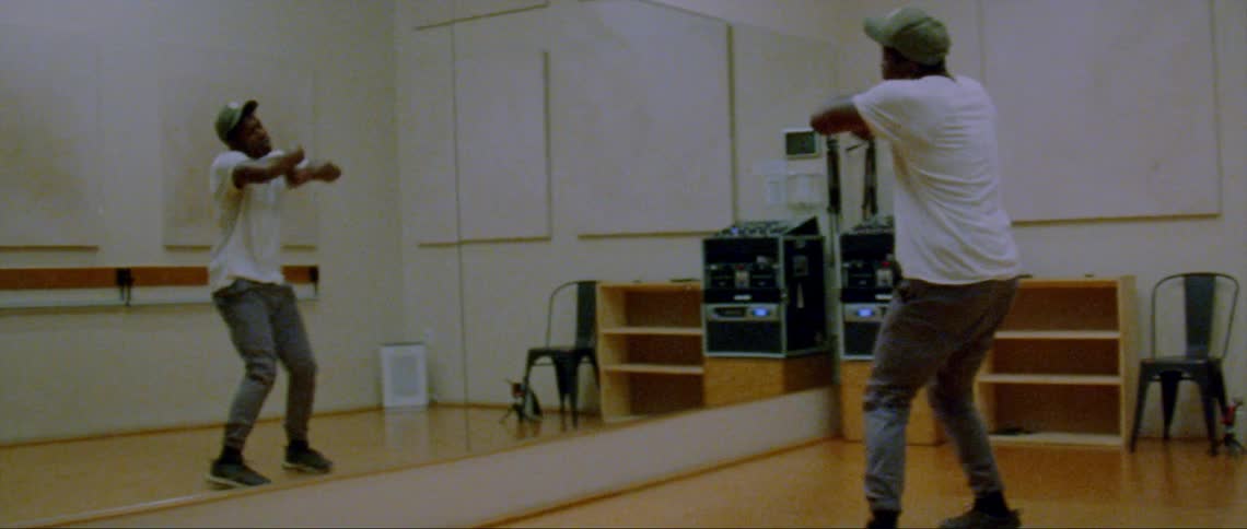 A young black man is dancing inside of a studio indoors