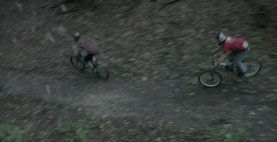 Two people riding and jumping bikes on a trail in the woods