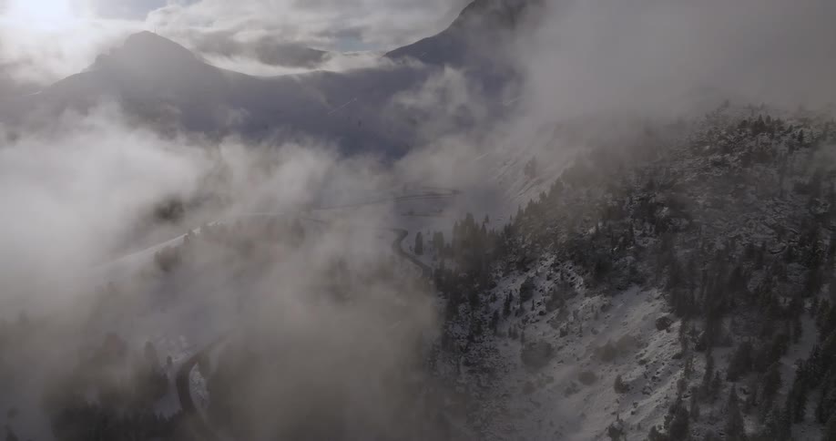 An aerial view of a road in a forest on a snowy mountain landscape in the morning with rising fog