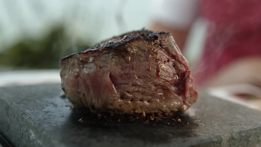 A person is cooking a piece of steak outdoors