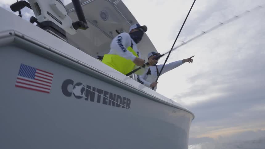 A view from the water of two men fishing and reeling in something on the boat