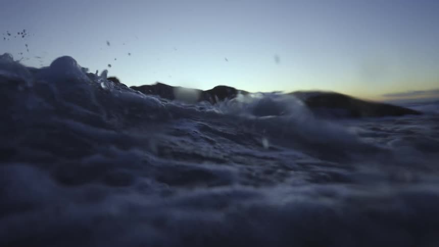An ocean wave splashing towards a shoreline at dusk