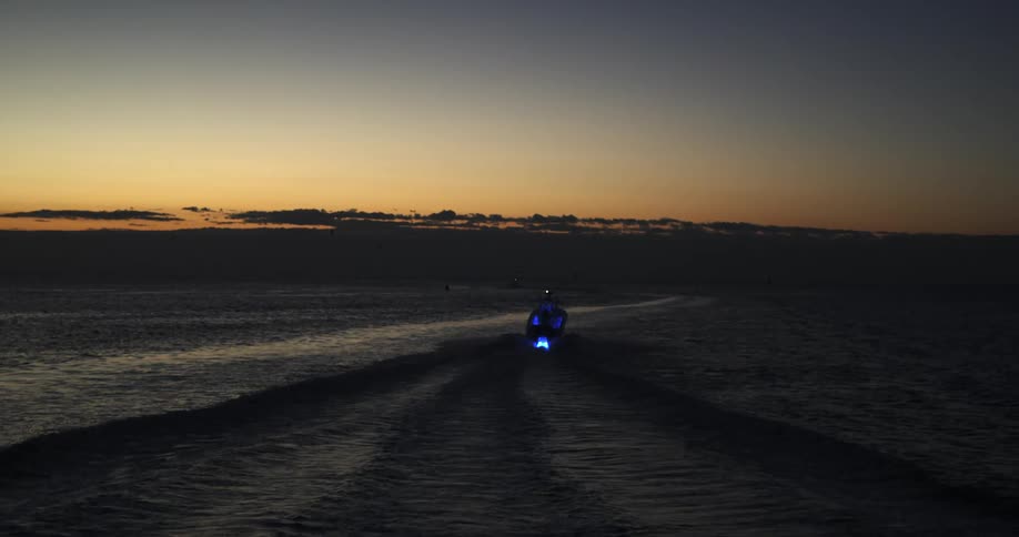 Lights on a small boat glow as it moves across the water as the sun has set and the sky grows darker