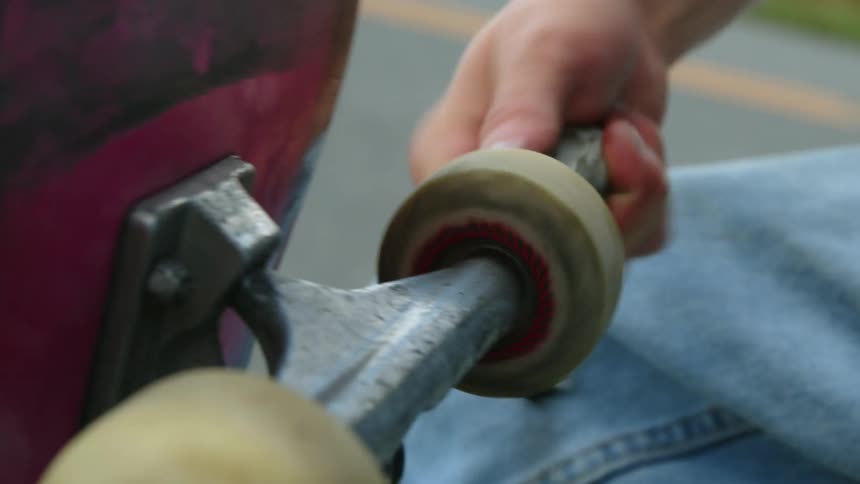 Man wearing jeans fixes skateboard wheel in the street