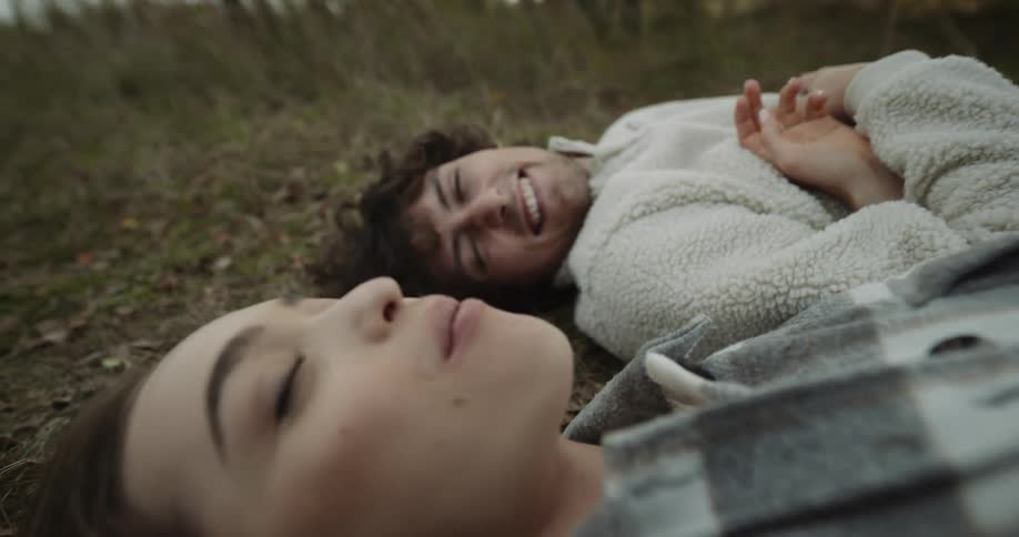 A man and a woman laying on the ground smiling at each other while the man puts food in the womans mouth