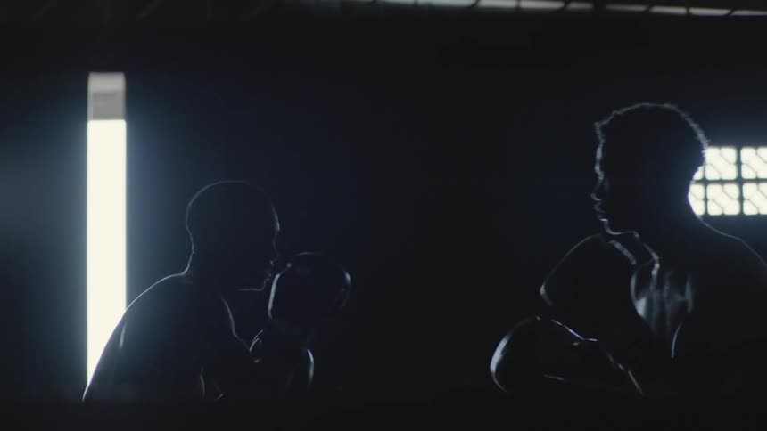 Two teenagers are boxing indoors against each other in a dimly lit boxing gym
