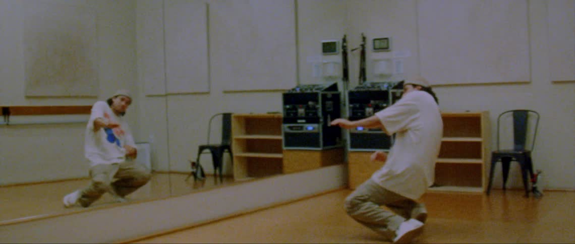 A young man dancing hip hop in front of a large mirror in a dance studio