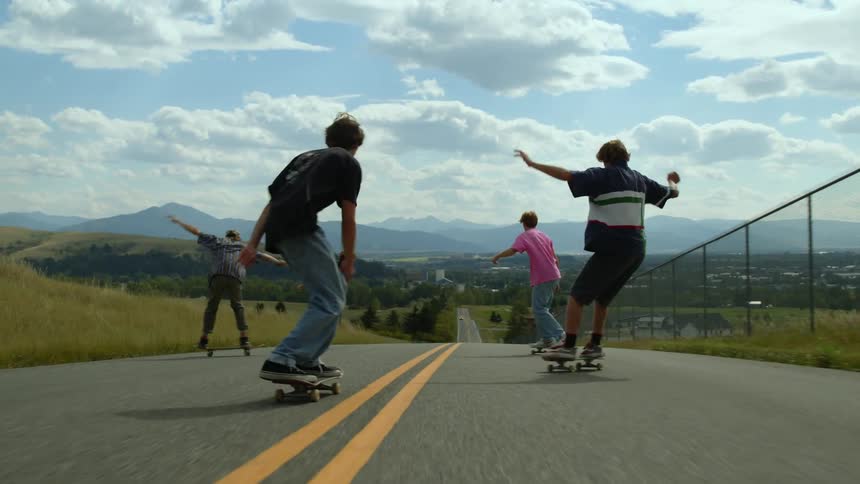A group of teenage boys skateboarding down a hillside road on a summer day