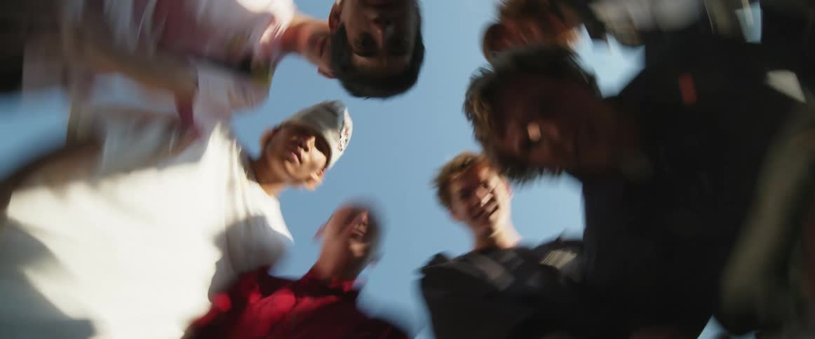 Time lapse of a group of teenage boys crouching and making faces into a spinning smartphone on a sunny day