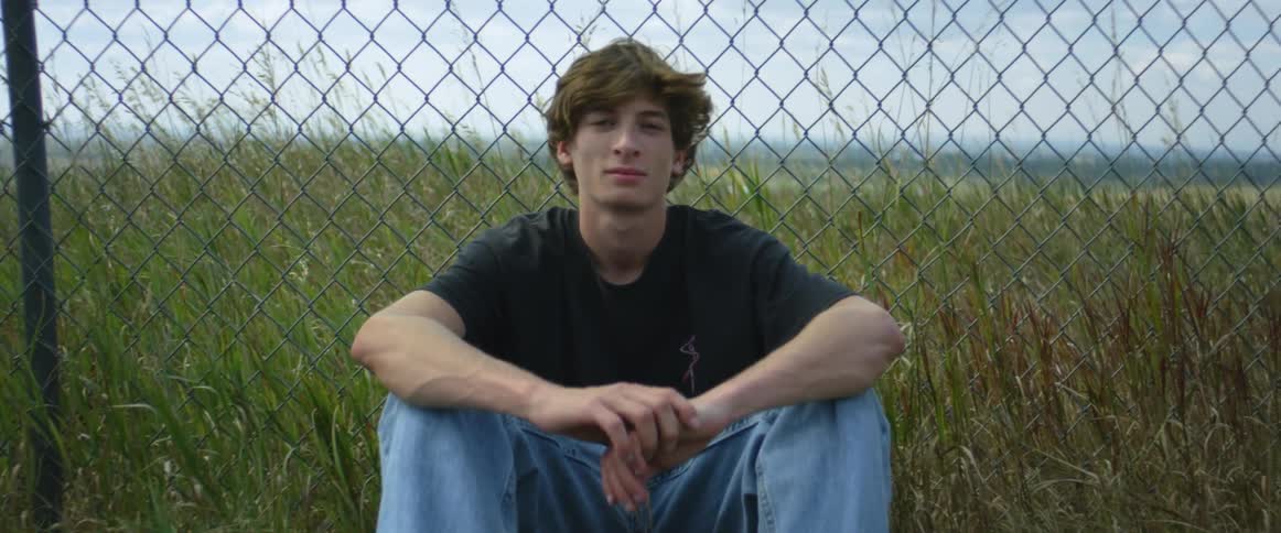 A teen is sitting by a fence in a grassland area