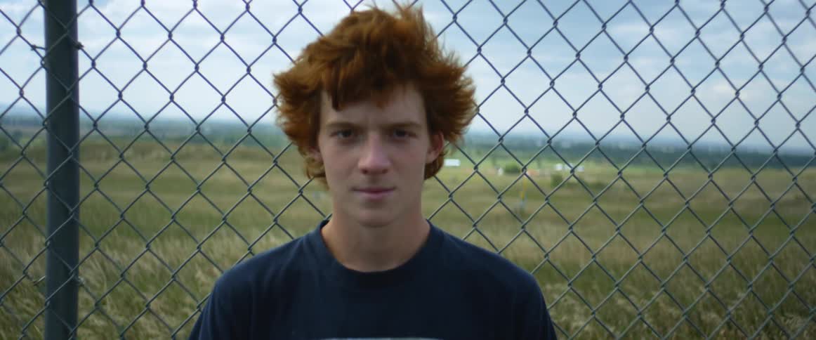 A teen is standing near a fence during the spring time