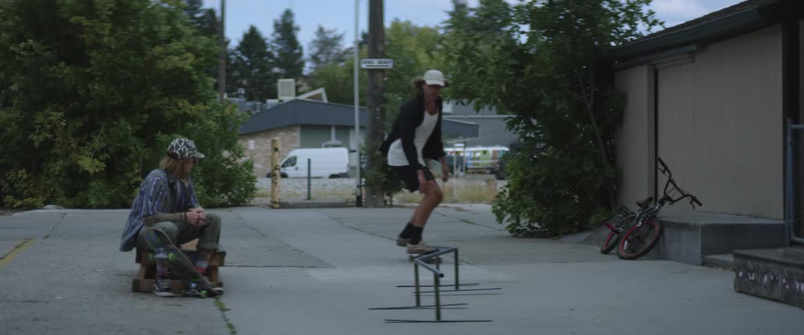 A man riding a skateboard and riding it on a rail while another man sits and watches