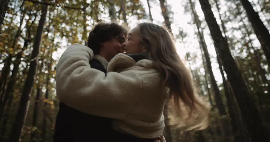 A woman and a man frolicking through the forest jumping into each others arms and then kissing