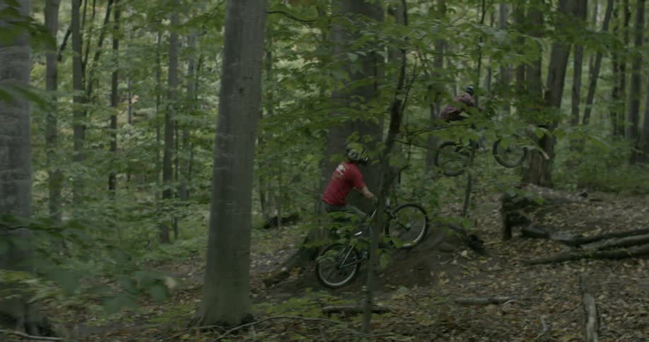 Two people ride a bike doing jumps in the forest