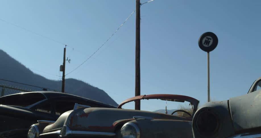 Classic cars sit parked side by side below rolling hills