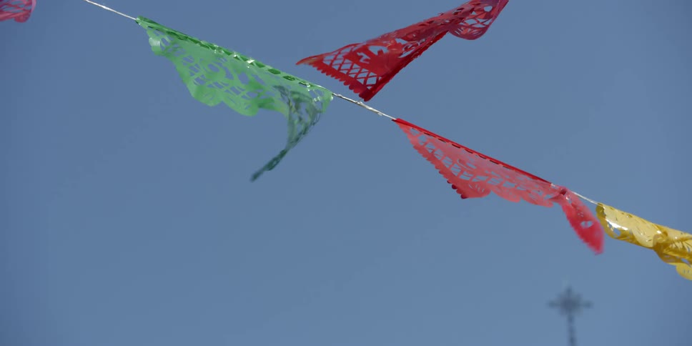 Colored flags hanging on a line are moving in the wind under a clear blue sky