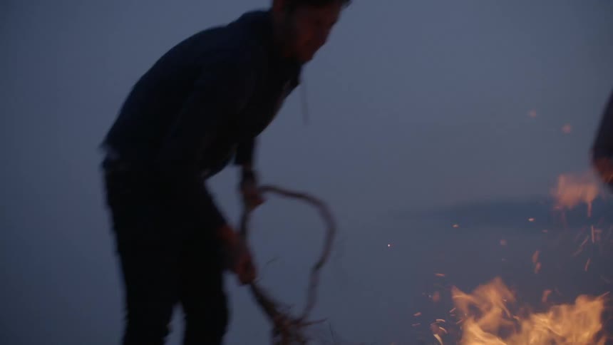 A man is stirring a fire on a beach