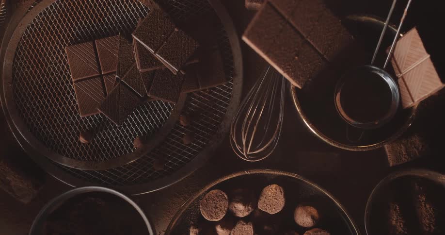 Smoke floats over a table with bowls and plates of cookies and chocolates and a wire whisk