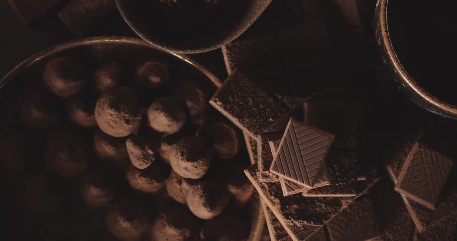 Chocolate candy is in a bowl on a table next to stacks of square chocolate cookies