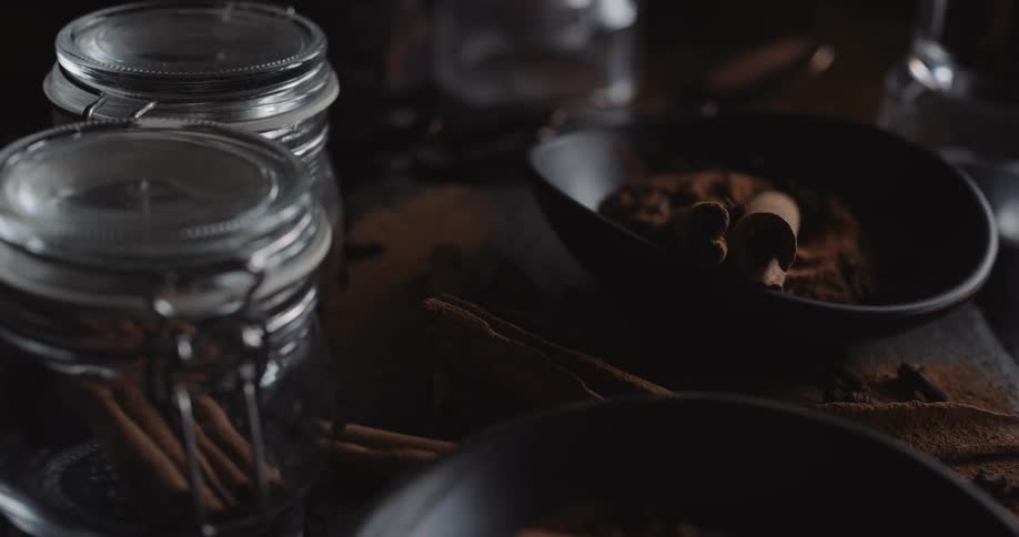Two cinnamon sticks in black bowlnext to jars and cinnamon powders on wooden table